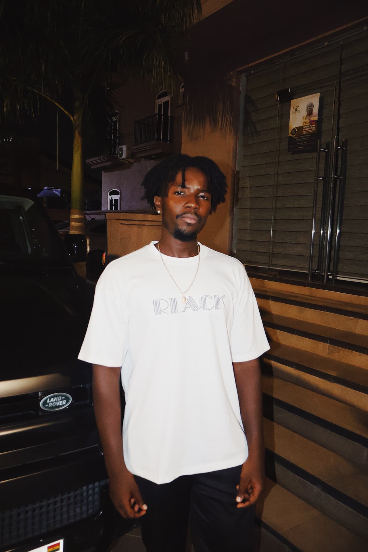Broni in a white t-shirt photographed at night beside a Land Rover