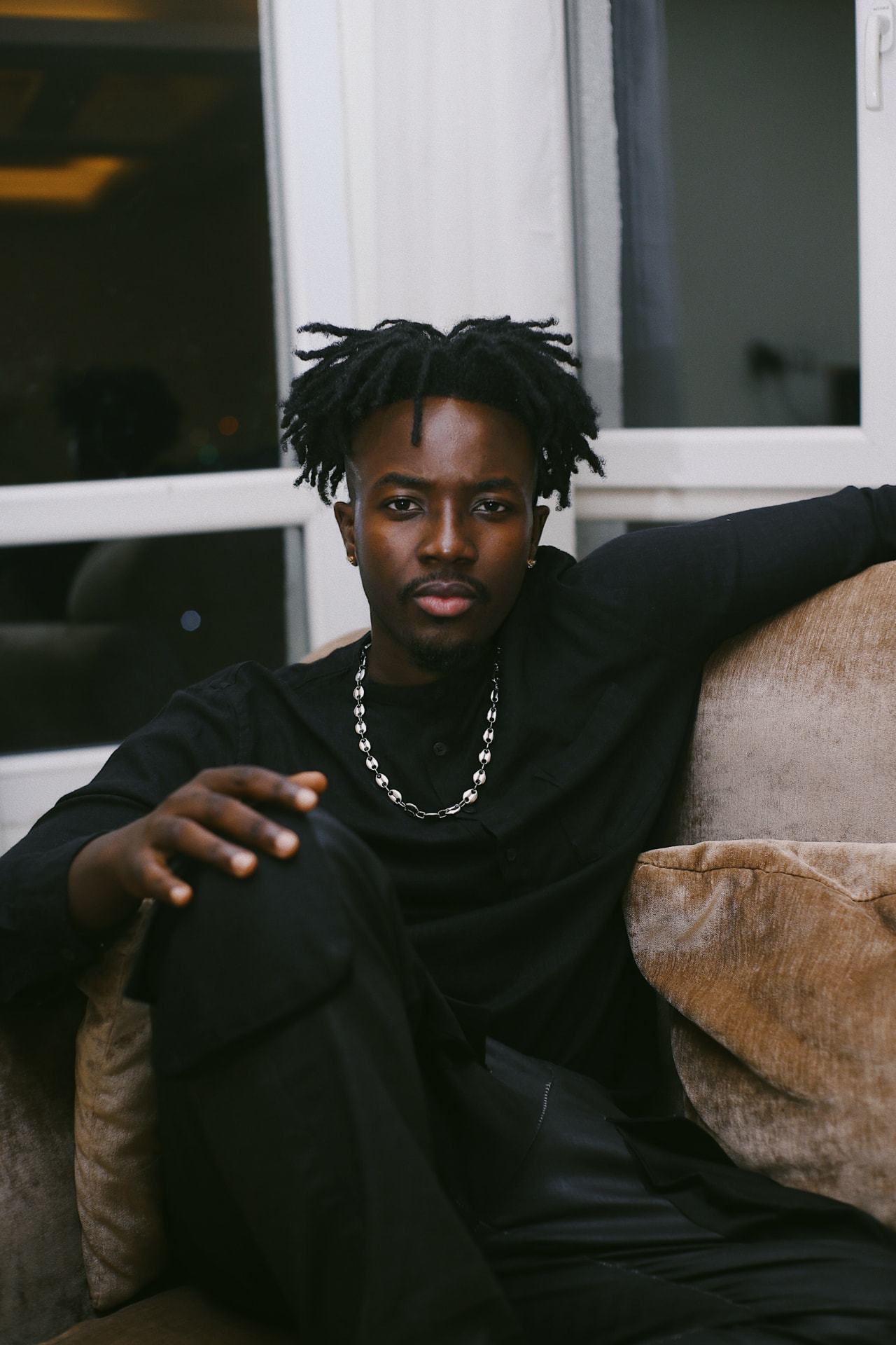 Broni lounging in a velvet armchair in an all-black outfit